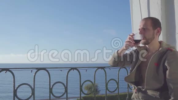甲正坐在阳台上在大海的背景上喝红酒特写镜头视频的预览图