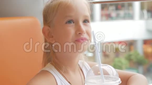 小女孩在咖啡馆喝牛奶鸡尾酒可可加牛奶孩子喝奶昔坐在咖啡馆里视频的预览图