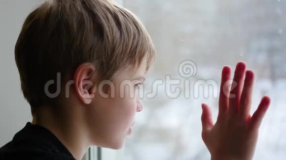 孩子坐在窗台上看着窗外的雪特写视频的预览图