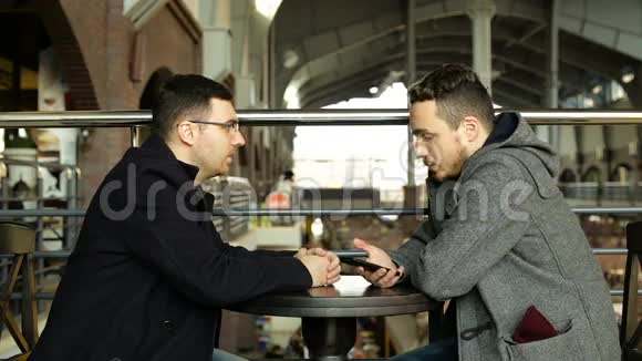 两个拿着智能手机的家伙在大商店咖啡馆里聊天视频的预览图