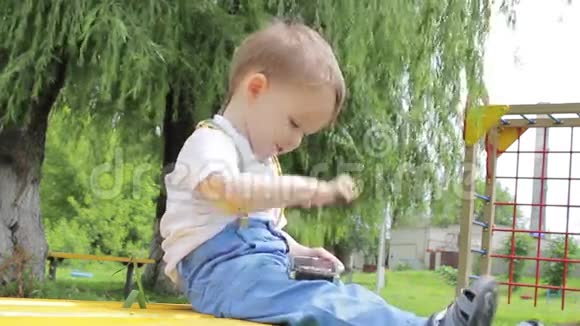 小男孩坐在操场上的长凳上玩着智能手机视频的预览图
