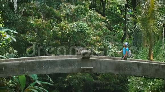 巴厘岛在岛上游览女孩走在石桥上深色头发的女人用一根自拍棒视频的预览图