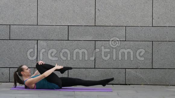 年轻运动女性做瑜伽和普拉提健身操灰城市背景和粉红色瑜伽垫视频的预览图