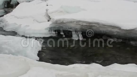河水流过冬天的冰雪清澈的水底部的石头视频的预览图