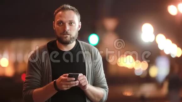 帅哥发短信用智能手机就走了街道上的城市灯光模糊现代技术视频的预览图