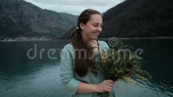 年轻女子捧着一束含羞草在湖边吸入芬芳视频的预览图
