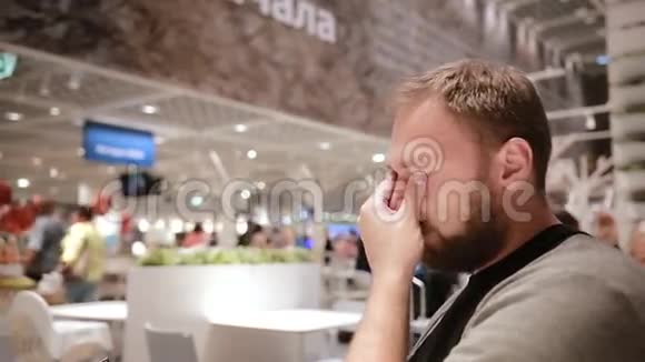 一个男人手里拿着智能手机坐在公共场所的侧视人摸了摸自己的脸现代技术视频的预览图