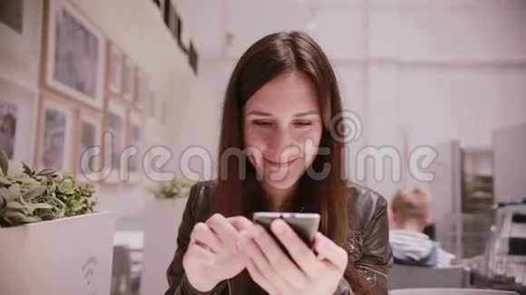 漂亮的年轻女人穿着皮夹克用她的智能手机说话微笑墙上的照片视频的预览图