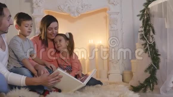 家庭阅读书籍坐在沙发前壁炉在圣诞节装饰的房子内部视频的预览图