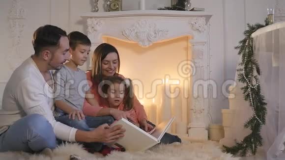 家庭阅读书籍坐在沙发前壁炉在圣诞节装饰的房子内部视频的预览图
