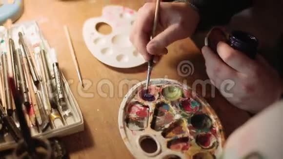 近距离观看男性艺术家的手在画画家用画笔混合调色板上的颜色视频的预览图
