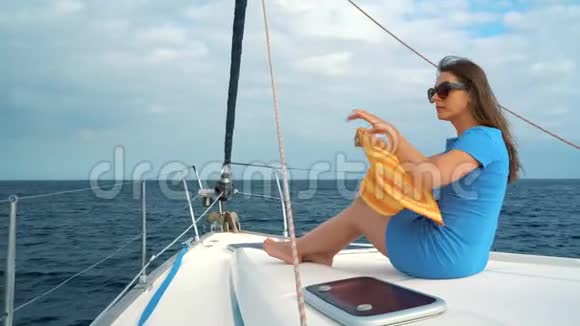 穿着黄色帽子和蓝色连衣裙的女人在海洋的夏天在游艇上挥舞着头发微笑着视频的预览图