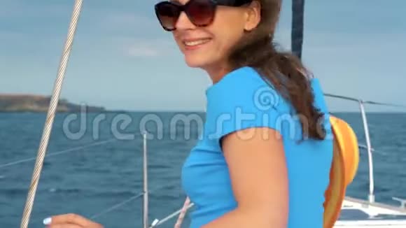 穿着黄色帽子和蓝色连衣裙的女人在海洋的夏天在游艇上挥舞着头发微笑着视频的预览图