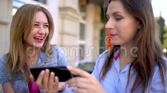 两个快乐的女人在咖啡馆里聊天和使用智能手机视频的预览图