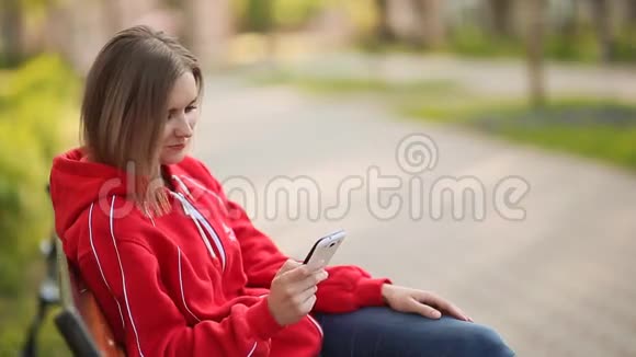 年轻女子坐在公园里的长凳上打着白电话视频的预览图