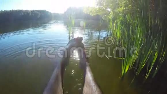 人在湖边或池塘边放松坐在木制码头的边缘在水中摆动一脚男腿视频的预览图