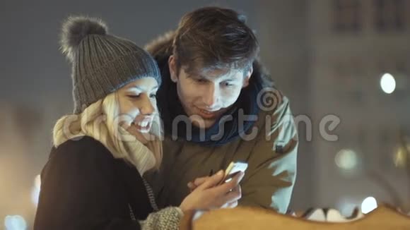 年轻夫妇晚上在一条城市街道上看智能手机上的照片视频的预览图