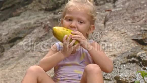 小金发女孩在石头上咬芒果视频的预览图