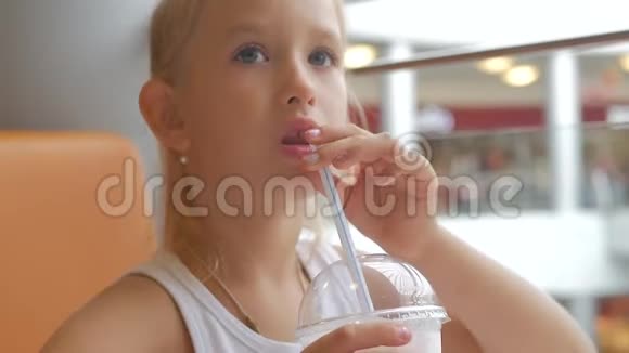 小女孩在咖啡馆喝牛奶鸡尾酒可可加牛奶孩子喝奶昔坐在咖啡馆里视频的预览图