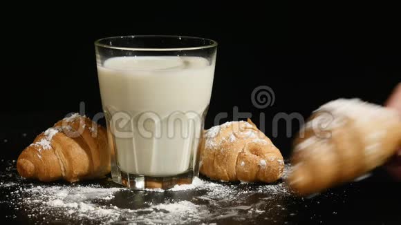 一杯牛奶黑色背景上有牛角面包手放羊角面包视频的预览图