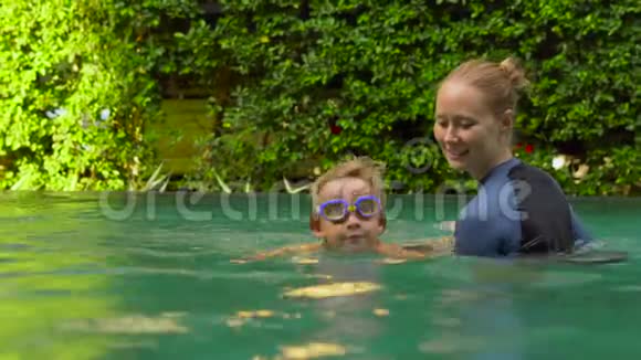 年轻女子游泳教练教一个蹒跚学步的男孩如何在游泳池里游泳视频的预览图