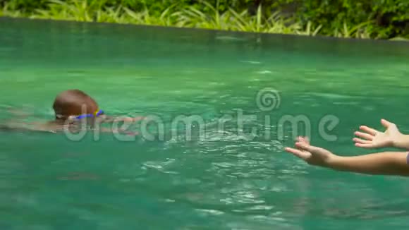 年轻女子游泳教练教一个蹒跚学步的男孩如何在游泳池里游泳视频的预览图