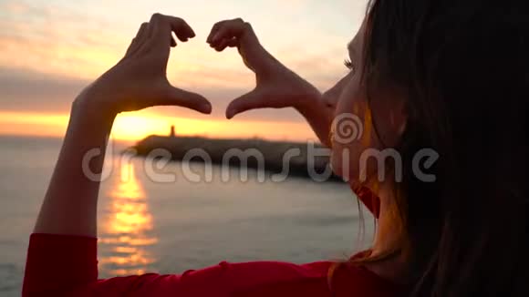 在海滩日落时用双手做心脏符号的女人视频的预览图