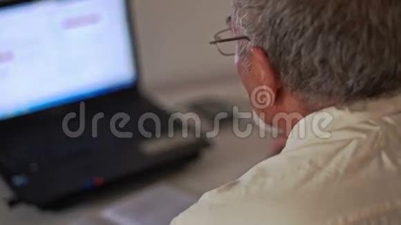 特写大胡子老人坐在桌上的笔记本前视频的预览图
