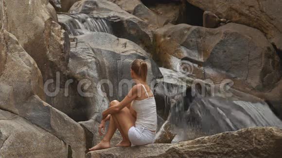 石头上的金发女郎看瀑布视频的预览图