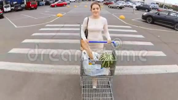 美丽的年轻女子在超市的停车场上走着车上装满了购物车视频的预览图