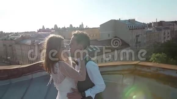 幸福的年轻漂亮时尚的夫妇新娘和新郎在日落城街道的屋顶上轻轻拥抱背景是视频的预览图