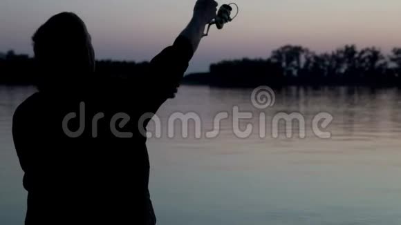 剪影渔夫在背景黄昏日落时在河中投掷鱼竿视频的预览图