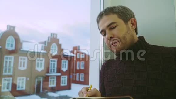 一位白发苍苍的年轻人在窗前的规划师上写着视频的预览图