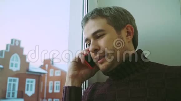 穿着毛衣的帅哥在窗户边对着联排别墅打电话视频的预览图