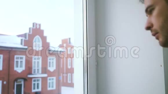 一位年轻的帅哥头发灰白透过窗户望着居民区视频的预览图