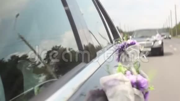 婚礼上的一束紫罗兰色的紫花在车上随风飘动幸福的新婚夫妇视频的预览图