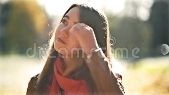 年轻美丽的女人在阳光明媚的日子里看着镜头秋天的背景微笑快乐女孩肖像视频的预览图