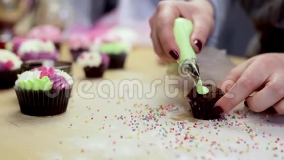 近距离观看女性手装饰巧克力纸杯蛋糕使用糕点袋与彩色奶油视频的预览图