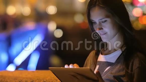 一个漂亮的黑发女人用她的平板电脑夜晚的城市背景上模糊的灯光慢悠悠视频的预览图