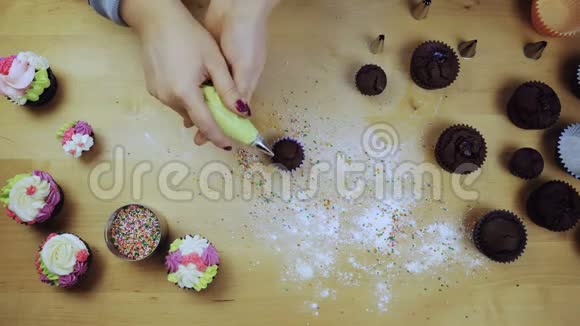 桌上巧克力蛋糕的俯视图年轻女子用糕点包里的彩色奶油装饰松饼视频的预览图