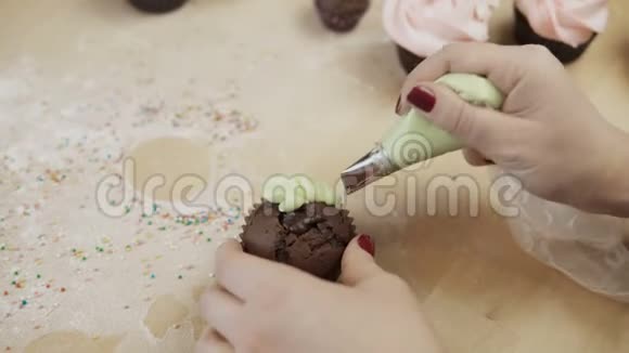 近距离观看女性手装饰巧克力纸杯蛋糕与彩色奶油使用糕点袋为此视频的预览图