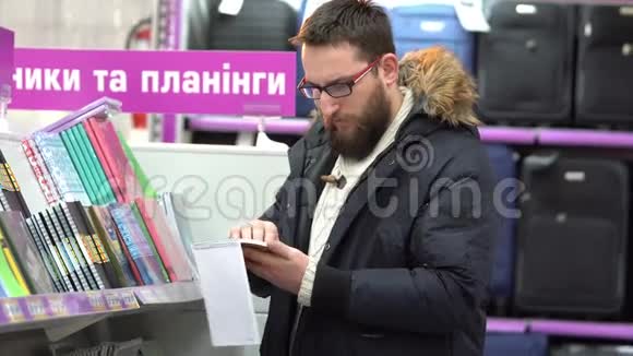 一个戴眼镜的年轻人在超市里挑选笔记本视频的预览图