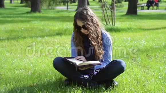 美丽的年轻女子坐在草地上的一个夏天的公园里读一本圣经视频的预览图