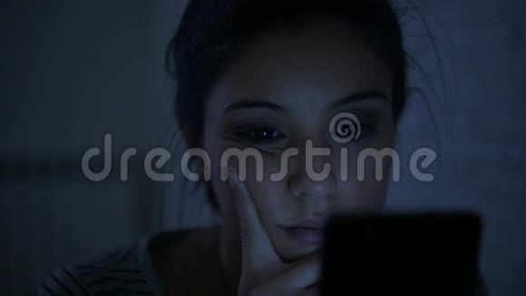 一个30多岁的西班牙裔年轻女子躺在床上深夜用手机看着侧着侧着的平底锅视频的预览图