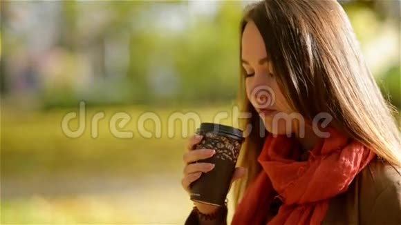 美丽的白种人年轻女子在秋天公园喝外卖咖啡秋天的漂亮女孩户外咖啡杯视频的预览图