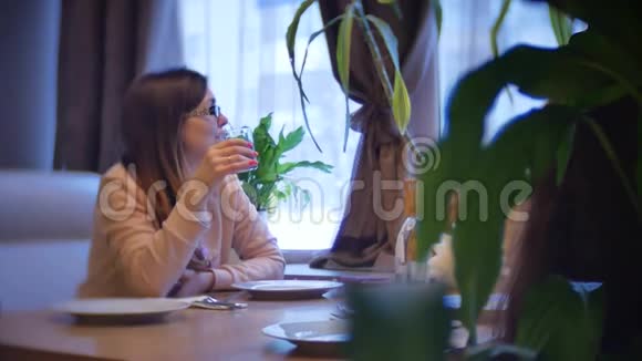 那个女人坐在咖啡馆里喝着一杯玻璃杯女人正在室内咖啡馆里吃一段慢动作视频视频的预览图