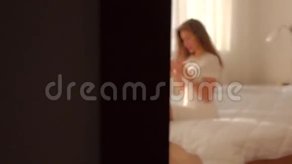 穿着白色裙子的年轻女子坐在床上用手机视频的预览图