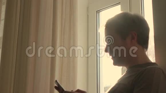 开朗的年轻人用他的智能手机靠窗4K型侧面射击视频的预览图