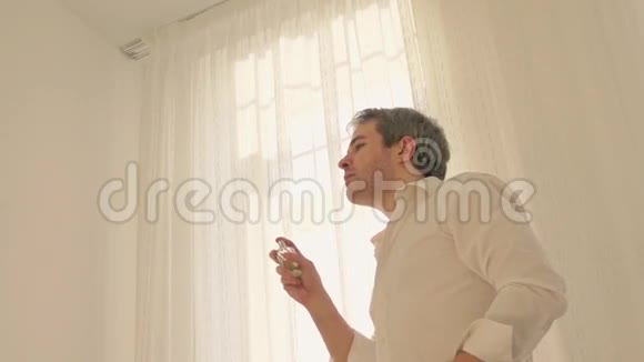 穿白色衬衫的人在阳光明媚的卧室里喷香水超级慢动作镜头视频的预览图