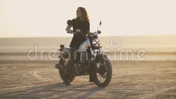 有魅力的年轻女摩托车手在摩托车上精疲力竭然后骑走日落或日出射向沙漠女司机视频的预览图